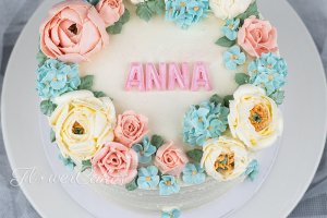 Tårta dekorerad med spritsade blommor och text.