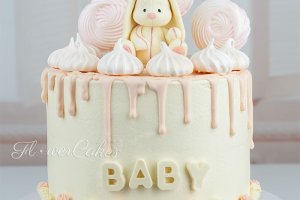 Babyshowertårta dekorerad med drip, en hare av choklad, maränger + maränger på pinne, samt lite glasstrutar - även de av choklad - kring botten av tårtan.