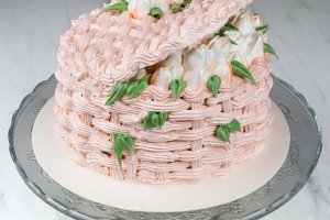 Tårta formad som en korg med locket på glänt och blommor inuti. Dessa blommor är spritsade av italiensk maräng.