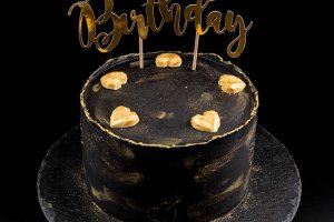 Födelsedagstårta av typen snickers, dekorerad med svart chokladganache med guldstänk, samt med guldhjärtan och en cake topper.
Prisgrupp: Avancerad dekor + tillägg för cake topper
