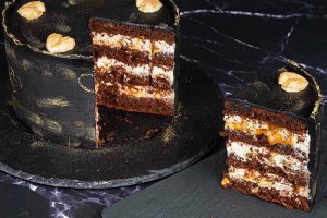 Födelsedagstårta av typen snickers, dekorerad med svart chokladganache med guldstänk, samt med guldhjärtan.