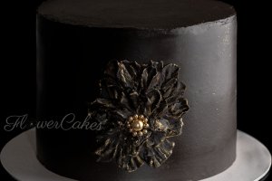Svart tårta, sparsamt dekorerad med en enda stor blomma med gulddetaljer.